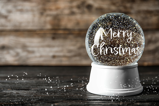 Beautiful snow globe with phrase Merry Christmas on wooden table. Space for text