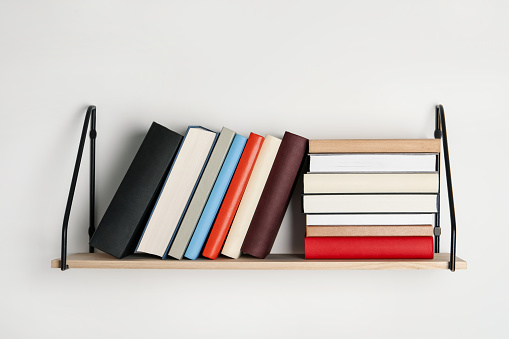 Wooden shelf with many hardcover books on white wall