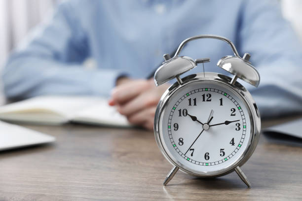 istock White alarm clock and man working at table, closeup. Space for text 1494650112