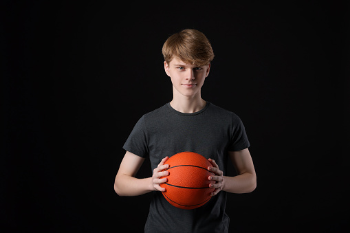 Teenage boy with basketball ball on black background