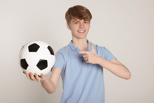 Teenage boy with soccer ball on light grey background