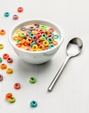 Bowl of colored cereal and spoon on a white wooden surface