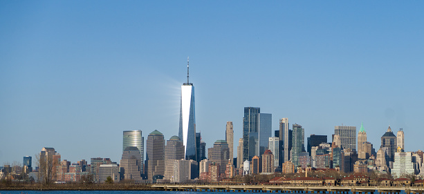 Buildings reflect the bright sunshine on a sunny, blue-sky day in New York City as seen from Liberty State Park