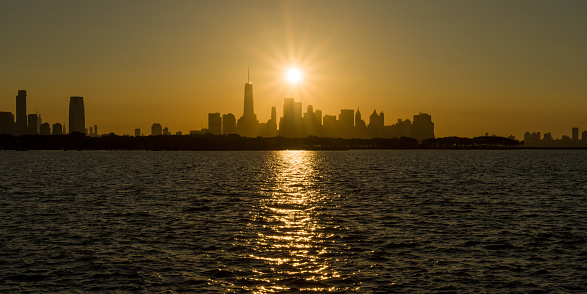 Very bright sun rises on a clear day in New York City. The sun is reflected off rough Hudson River heavily contrasting the choppy river with the clear skies