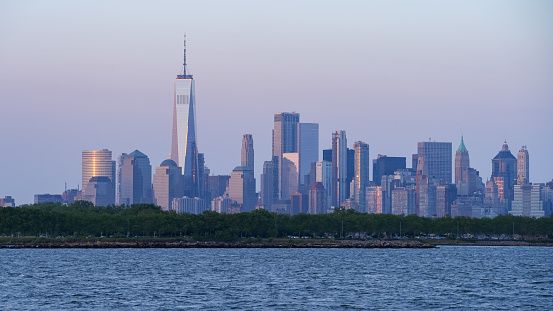 As the sun sets over New York City - with Liberty State Park in the foreground, the clear sky takes on a purple tint, giving the buildings a purple hew.
