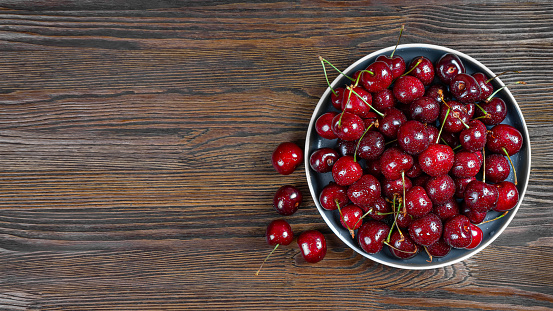 Fresh red ripe sweet cherry with water drops on plate on brown wooden background. Berry, food background. Top view, banner, header with copy space.