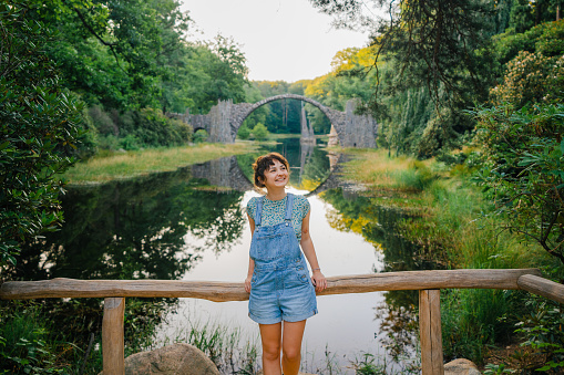Young Caucasian woman in denim short overalls on the background of the Devil's Bridge