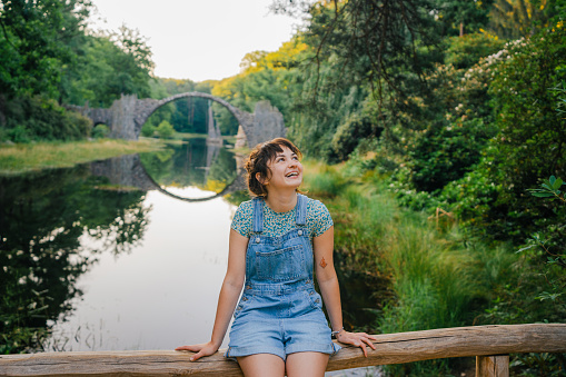 Young Caucasian woman in denim short overalls on the background of the Devil's Bridge