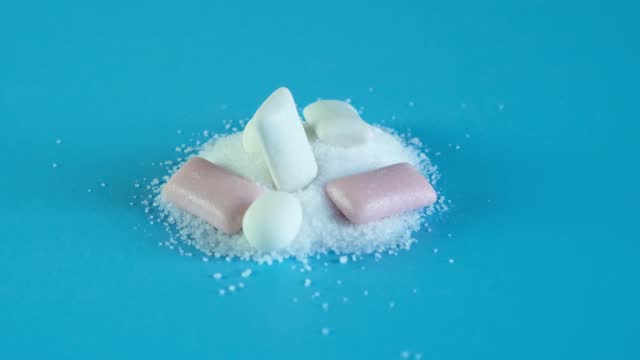 Chewing gum and tooth-friendly sweets with xylitol on slide of crystalline xylitol powder. Video, rotational movement. Concept - dental health. Sugar substitute, Xylit. Food additive, E967