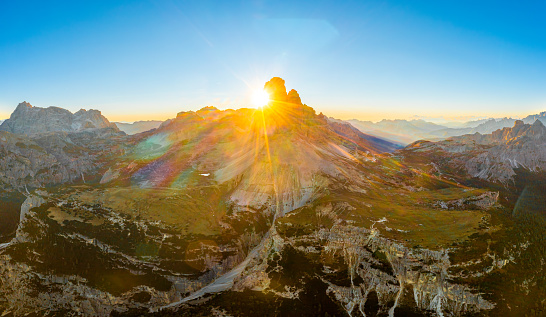 Landscape of Three Peaks of Lavaredo. Sunny rocky mountain ranges and hilly canyons under blue sky with white clouds at sunrise aerial view