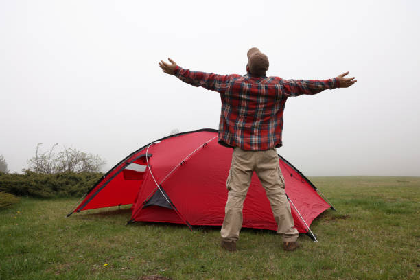 Man raises arms in front of tent where he is camping