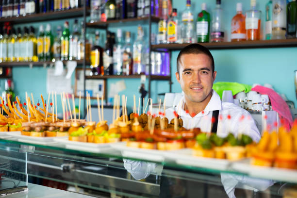 Friendly young male bartender offering appetizing pinchos in pub