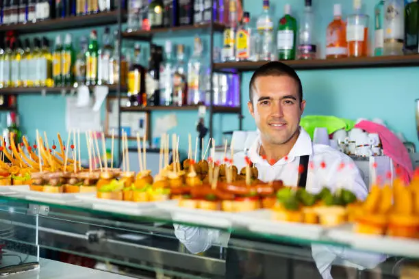 Photo of Friendly young male bartender offering appetizing pinchos in pub