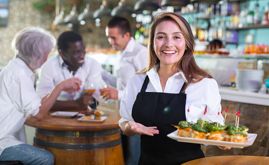Positive female waiter holding tray with pinchos at restaurant