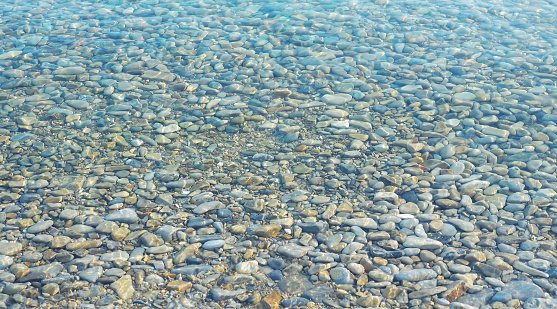 Photo of a calm transparent water surface with pebbles under water surface.