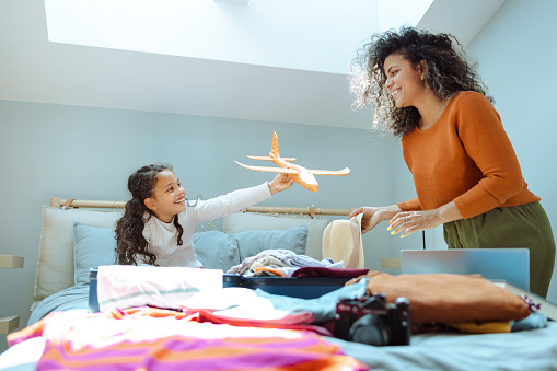 Beautiful Latin woman smiling and preparing for a trip. Little girl is playing with airplane toy