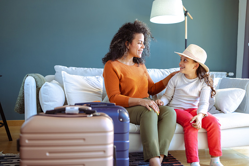 Beautiful Latin woman smiling and talking with her daughter. They are sitting on the sofa. Suitcases are in the foreground