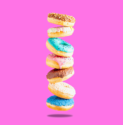 Sweet donuts of different colors in flight on a pink background