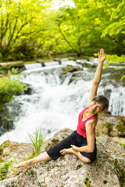 istock A woman performing yoga stretching on a rock by a waterfall 1494669373