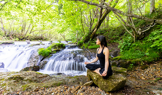 A mid age woman meditating by herself in nature by a waterfall.