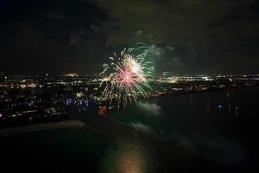 Aerial view of bright fireworks exploding with colorful lights over sea shore on US Independence day holiday.