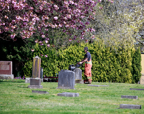 New Westminster, British Columbia, Canada- May 2,2023: Cemetery groundskeeper cutting the grass in a beautiful Spring setting