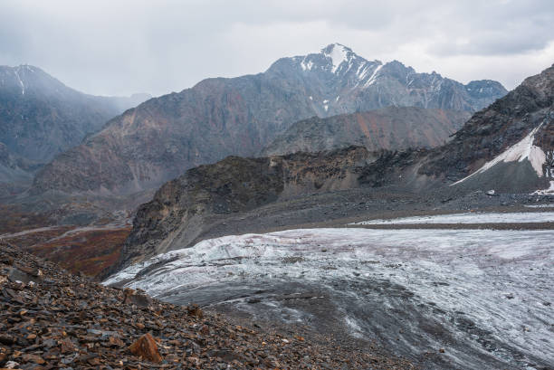istock Awesome landscape with long glacier tongue against high mountain range with sharp rocky peaked top in overcast weather. Cone shaped pointy peak in dramatic cloudy sky. Large glacier among sharp rocks. 1494676766