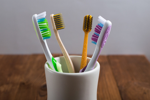 Toothbrushes for the whole family in a white ceramic cup on the wooden table. Healcare concept