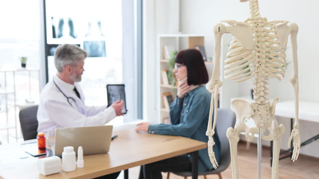 Skeleton in exam room of hospital with people in background