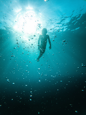 Full length shot of cute white child enjoying a swim. Underwater shot of blue ocean and child silhouette.