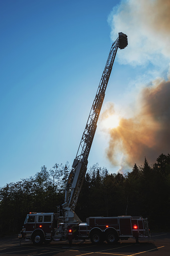 A firefighter surveys a devastating wildfire from the top of a truck ladder.