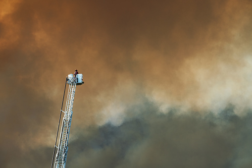 A firefighter surveys a devastating wildfire from the top of a truck ladder.