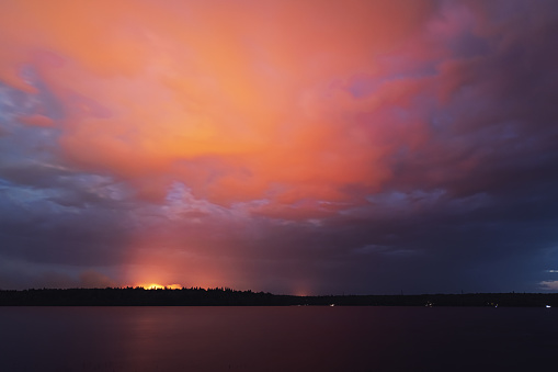 The flames of a distant forest fire illuminate clouds above a lake.