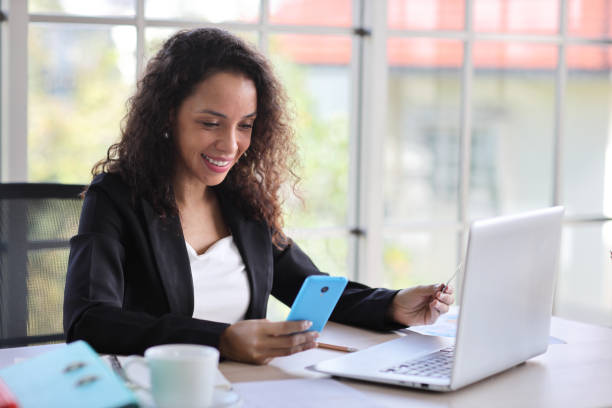 istock Attractive professional latin female employee worker sitting, using laptop computer with paperwork at home workplace. Businesswoman using smart mobile phone while holding credit card. 1494683738