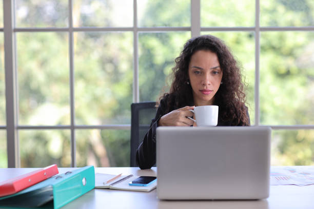 istock Attractive professional latin female employee worker sitting, using laptop computer while drinking coffee at home workplace. Businesswoman working on paperworks and communicate with client. 1494683745