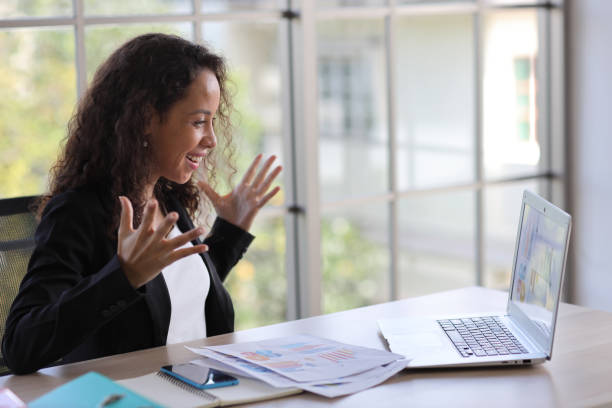 istock Attractive professional latin female employee worker sitting, using laptop computer with smart mobile phone at home workplace. Businesswoman working on paperwork while looking at camera and smile 1494683855
