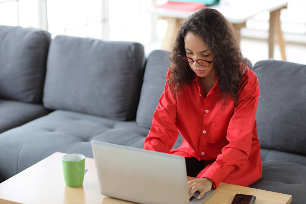 istock Smart and active latin woman sitting on sofa and using internet on computer with smart mobile phone while drinking coffee in living room. Lifestyle with technology 1494686752