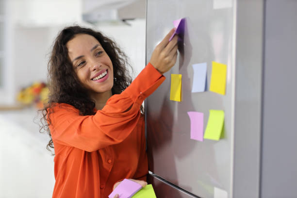 istock Smart and active latin woman standing and holding different colored sheets of note papers, ready for message on refrigerator in kitchen. Anywhere can work, lifestyle with technology concept 1494689181