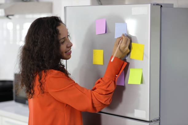 istock Smart and active latin woman standing and holding different colored sheets of note papers, ready for message on refrigerator in kitchen. Anywhere can work, lifestyle with technology concept 1494689230