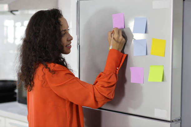 istock Smart and active latin woman standing and holding different colored sheets of note papers, ready for message on refrigerator in kitchen. Anywhere can work, lifestyle with technology concept 1494689231