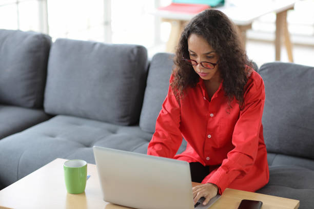 istock Smart and active latin woman sitting on sofa and using internet on computer with smart mobile phone while drinking coffee in living room. Lifestyle with technology 1494692230