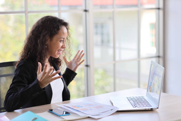 istock Attractive professional latin female employee worker sitting, using laptop computer with smart mobile phone at home workplace. Businesswoman working on paperwork while looking at camera and smile 1494692517