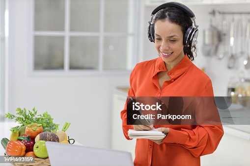 istock Happy latin woman learn cooking food while checking recipe from internet with computer in kitchen. Young female with headphone prepare delicious meal and listen music. Healthy and lifestyle concept 1494693159