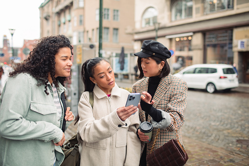 Close up of Three young women using a phone on a city street