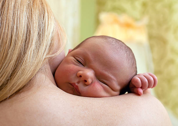 Newborn baby sleeping on mother's shoulder stock photo