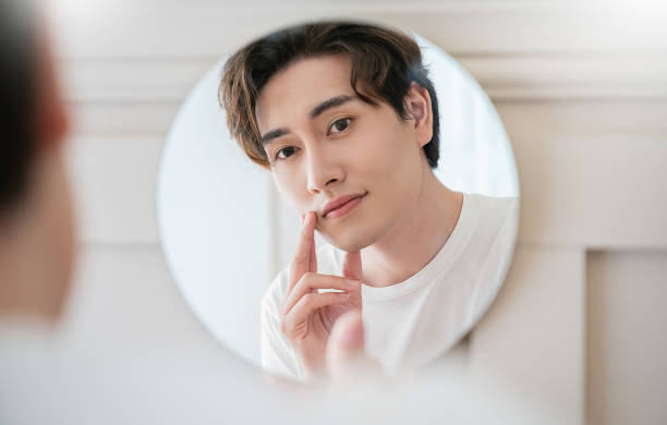 istock Closeup portrait of handsome beautiful asian boy with mirror makeup routine with copy space. Beauty influencer guy with perfect glow hand touch skin dress up. Healthcare man lifestyle cosmetic blogger 1494710793
