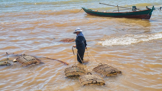 Sihanoukville, Cambodia - March 6, 2012. A Cambodian woman preparing to set traditional homemade bamboo fish traps in shallow water in the Gulf of Thailand.