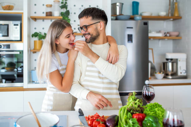 istock Beautiful young couple is looking at each other and feeding each other with smiles while cooking in kitchen at home. Loving joyful young couple embracing and cooking together, having fun in the kitchen 1494730608