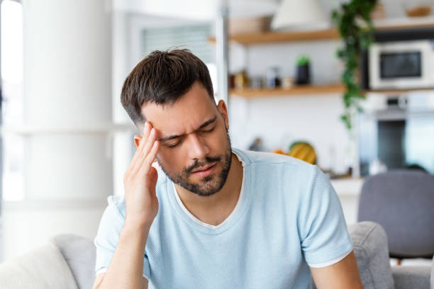 istock Man at home having a headache. Young man suffering from headache after hard working day, sitting on couch at home 1494730820