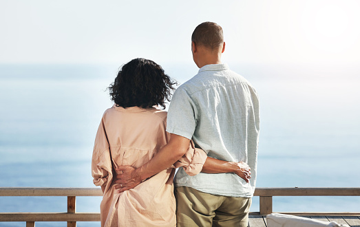 Back, view and senior couple by beach, hug and enjoying quality time on holiday or vacation. Love, care and retired elderly man and woman hugging, embrace or cuddle while having fun by ocean or sea.